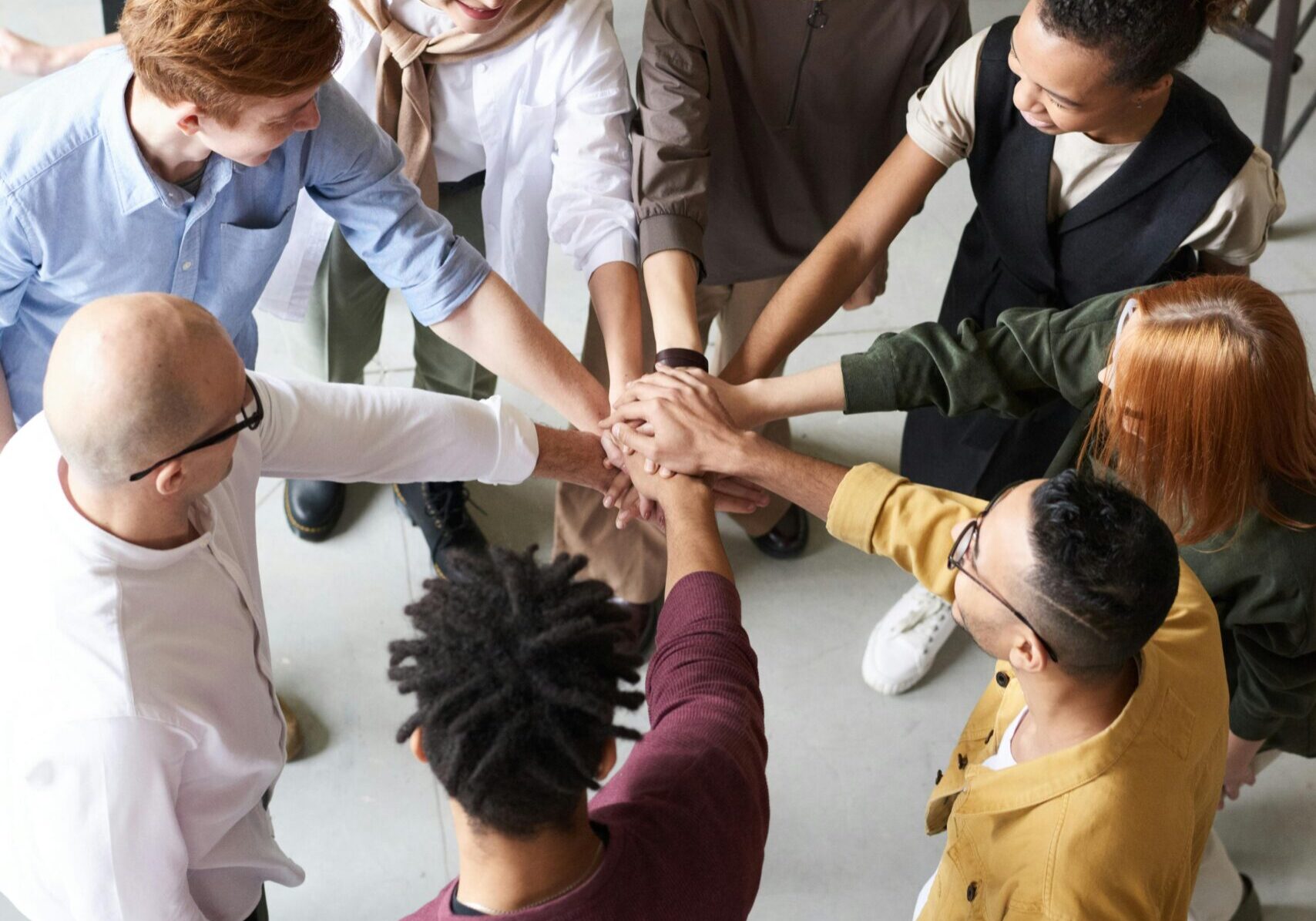 A diverse group of professionals joins hands in a team-building exercise indoors.